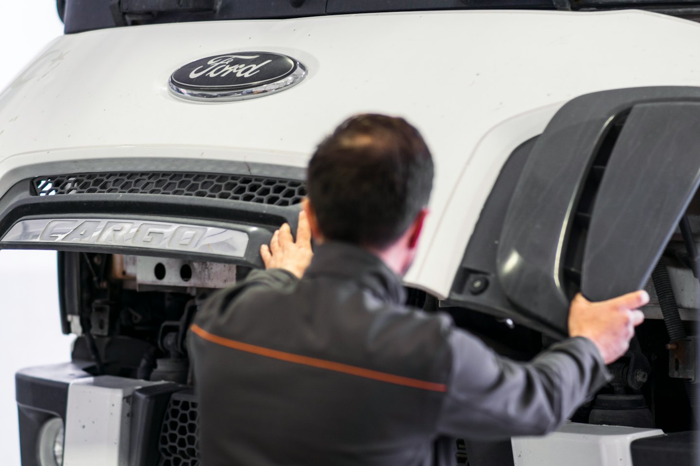 Technician working on the front grille of a white commercial truck.