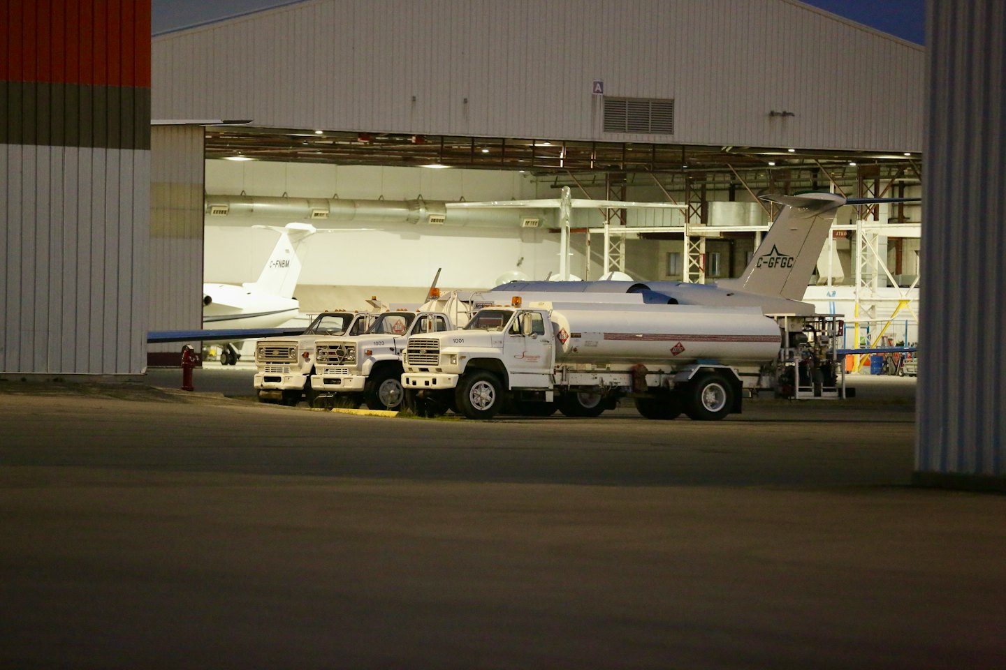 Fuel trucks park in front of an airport hangar with jets.